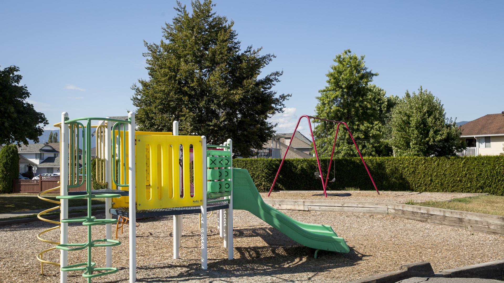 A small playground sits in the center of a bark mulch enclosure.